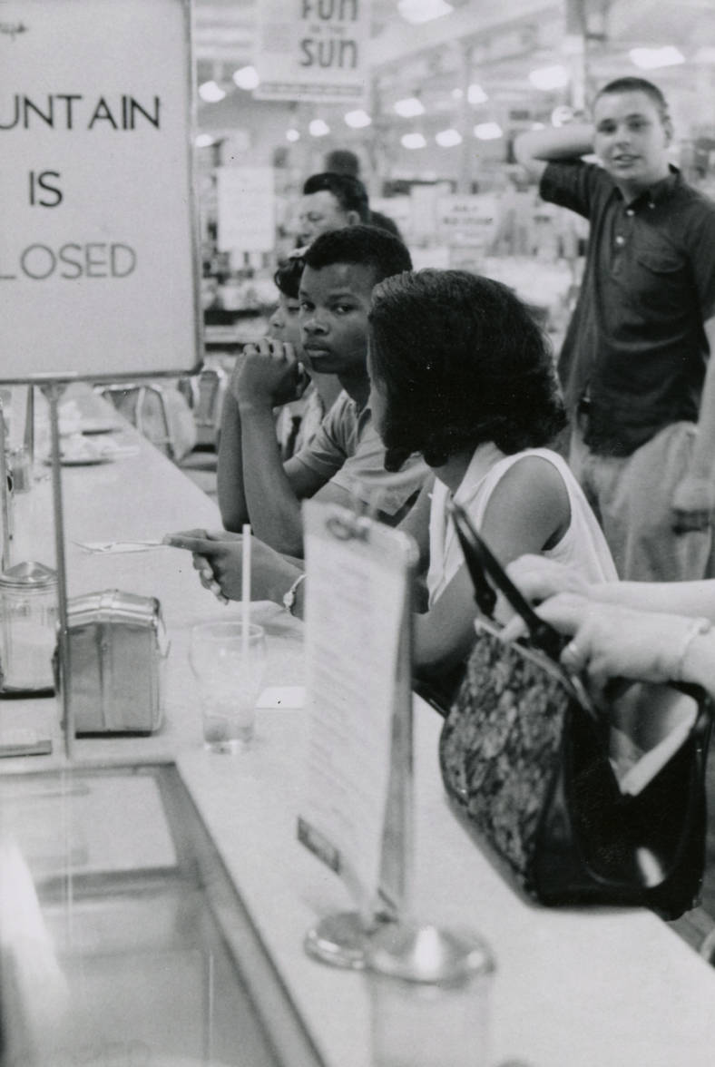 An image of African American students staging a sit-in at a lunch counter, overlooked by a white teenager